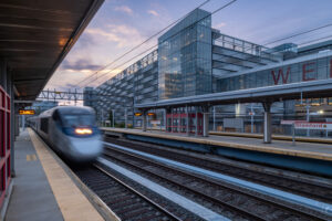 A train passes through the Stamford train station with the Stamford Transportation Center parking structure behind it
